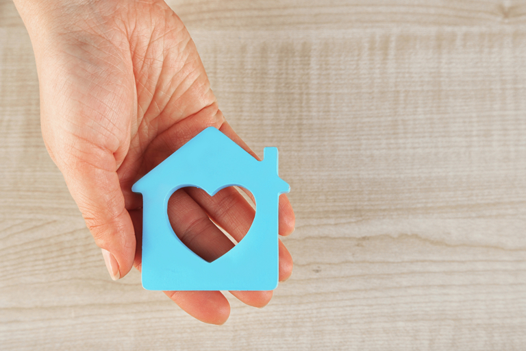 Female hand with model of house on wooden table background